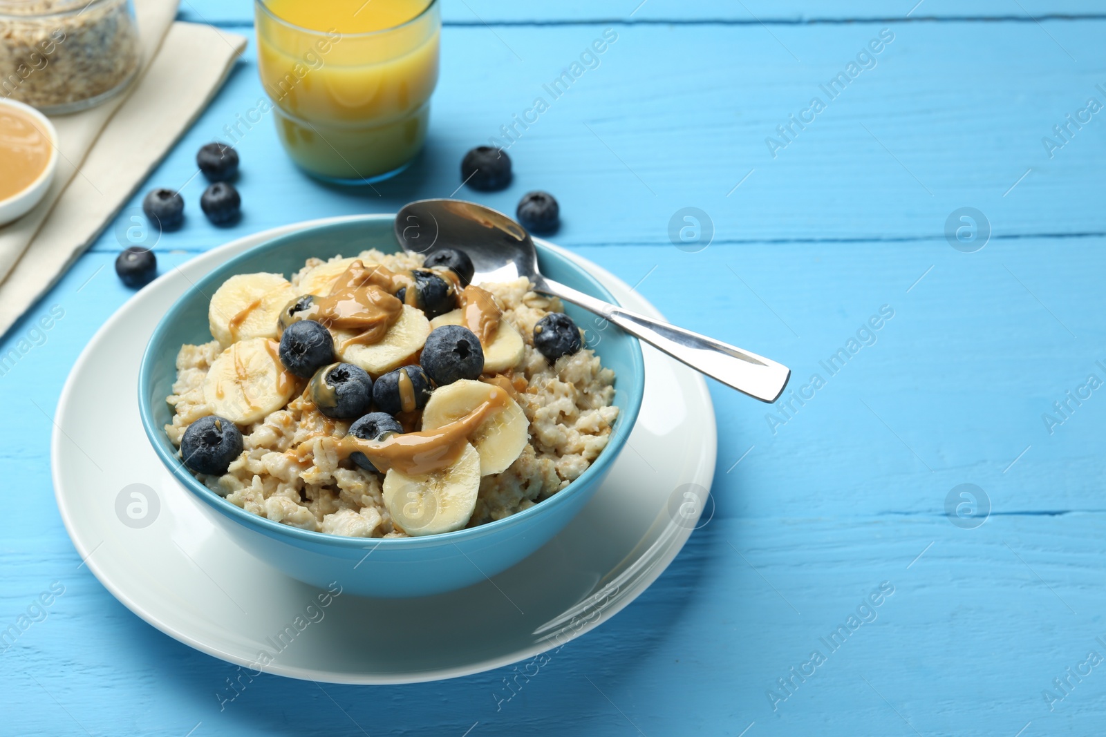 Photo of Tasty oatmeal with banana, blueberries and peanut butter served in bowl on light blue wooden table, space for text
