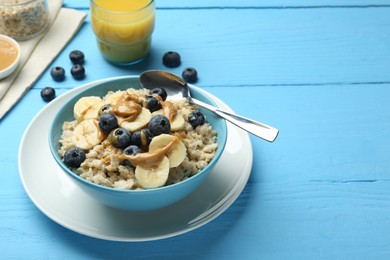 Photo of Tasty oatmeal with banana, blueberries and peanut butter served in bowl on light blue wooden table, space for text