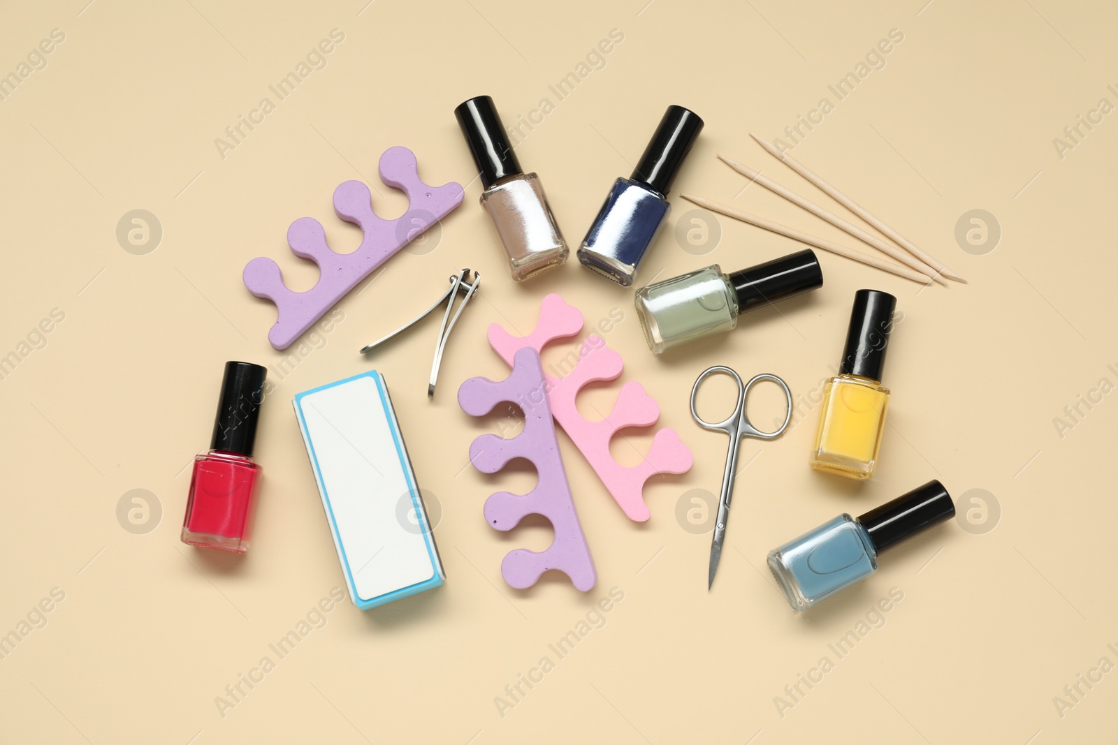 Photo of Nail polishes and set of pedicure tools on beige background, flat lay