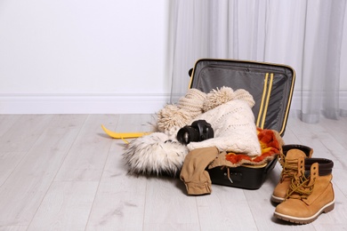 Open suitcase with warm clothes for winter vacation on wooden floor. Space for text