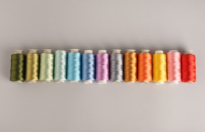 Photo of Different colorful sewing threads on light grey background, flat lay