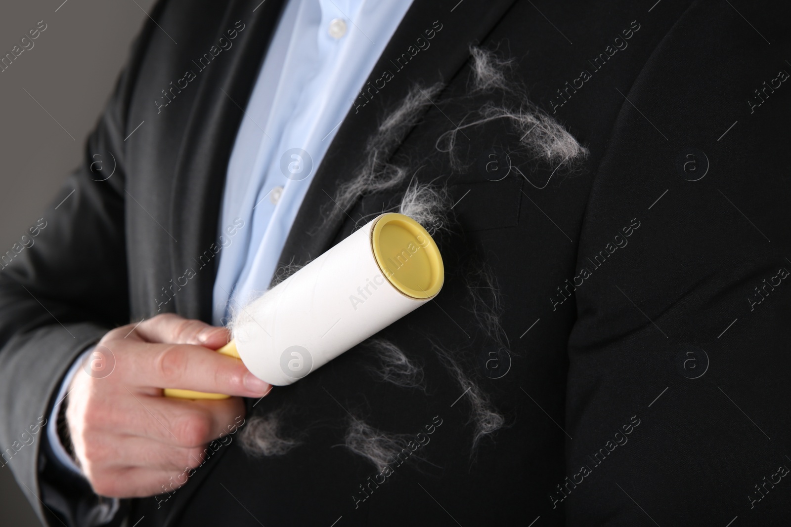 Photo of Man removing hair from black jacket with lint roller on grey background, closeup