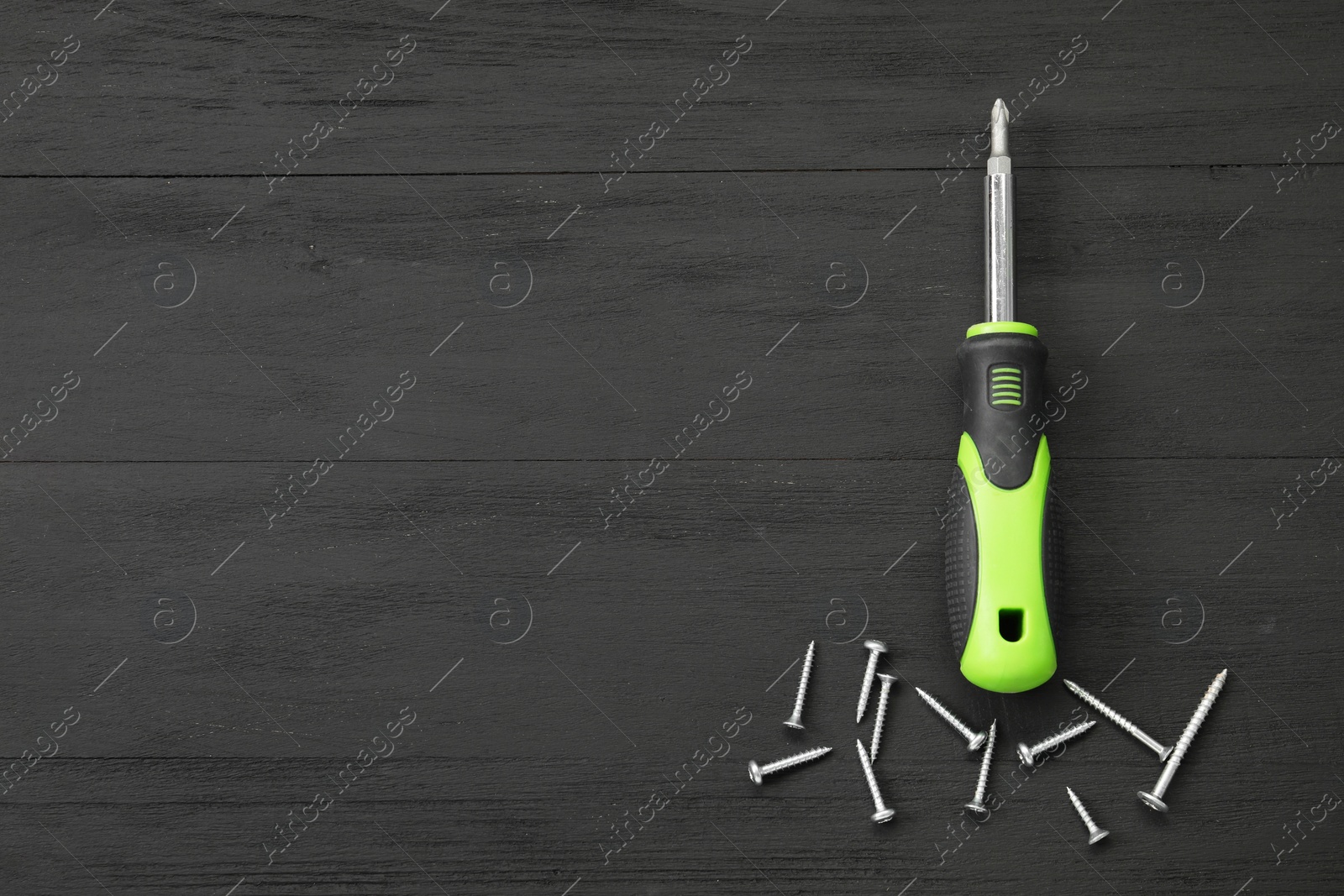 Photo of Screwdriver with green handle and screws on black wooden table, flat lay. Space for text