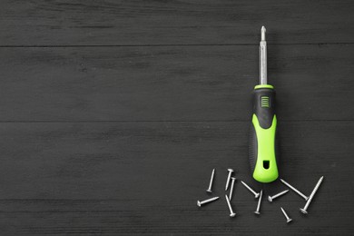 Photo of Screwdriver with green handle and screws on black wooden table, flat lay. Space for text