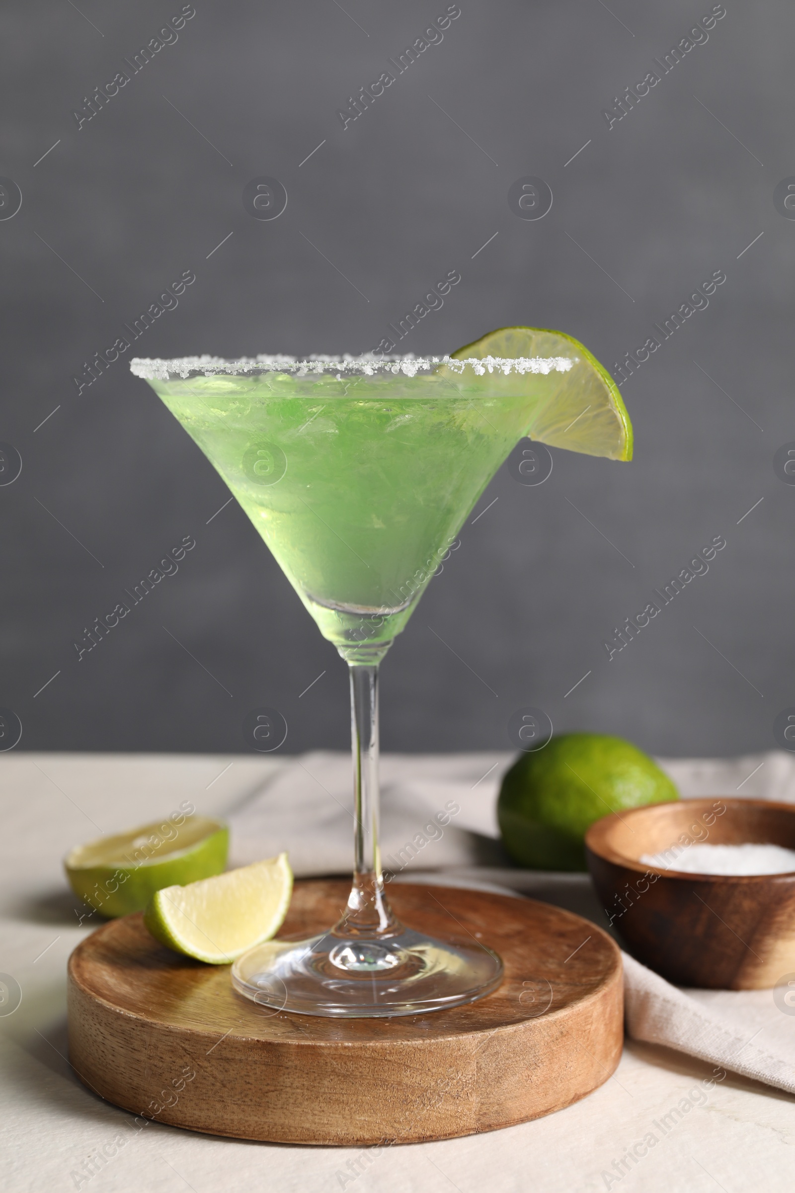 Photo of Delicious Margarita cocktail in glass, limes and salt on light table