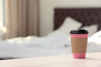 Cardboard cup of coffee on table in bedroom. Space for text