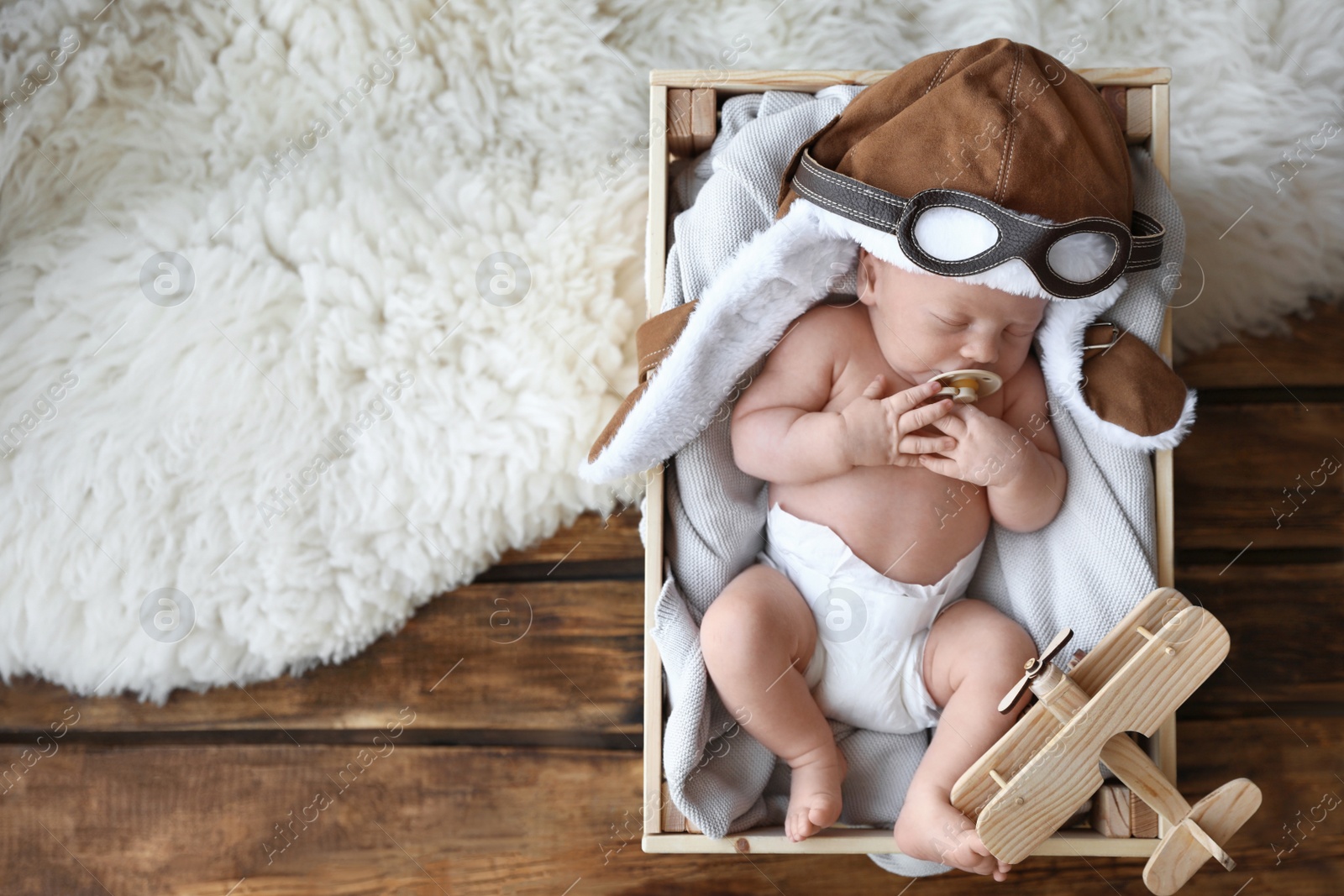 Photo of Cute newborn baby wearing aviator hat with toy sleeping in wooden crate, top view. Space for text