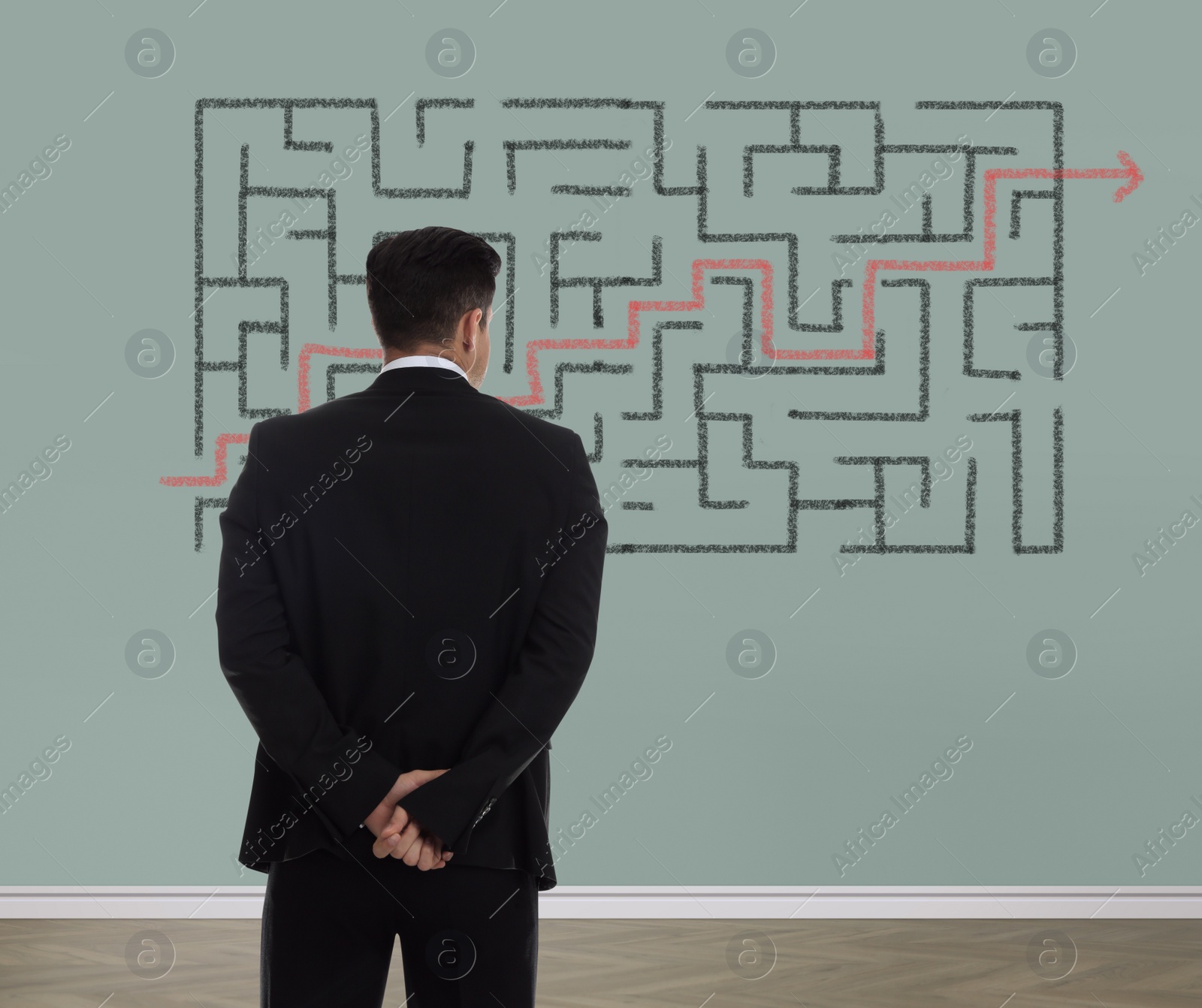 Image of Businessman looking at wall with illustration of maze indoors