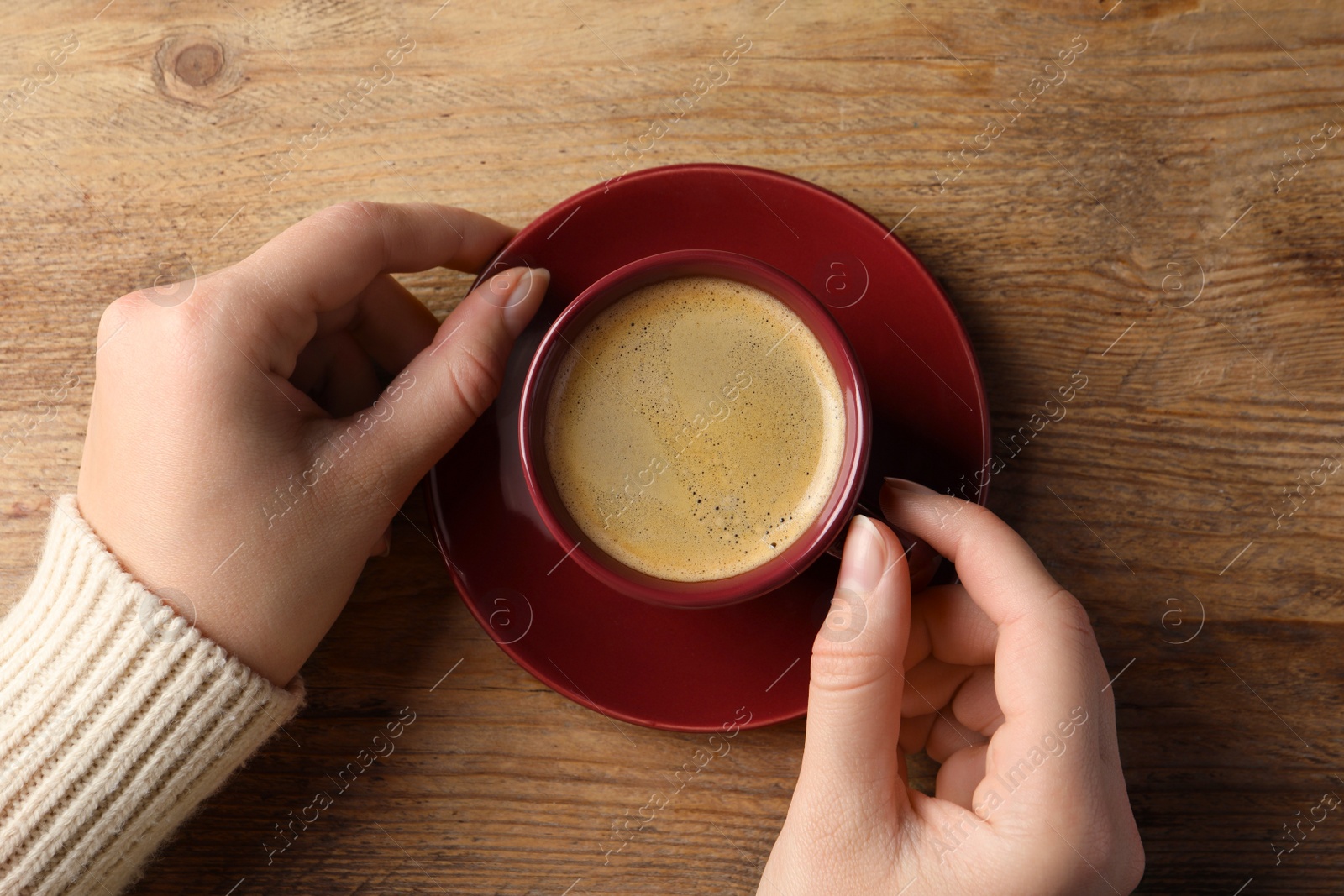 Photo of Woman with cup of hot aromatic coffee at wooden table, top view