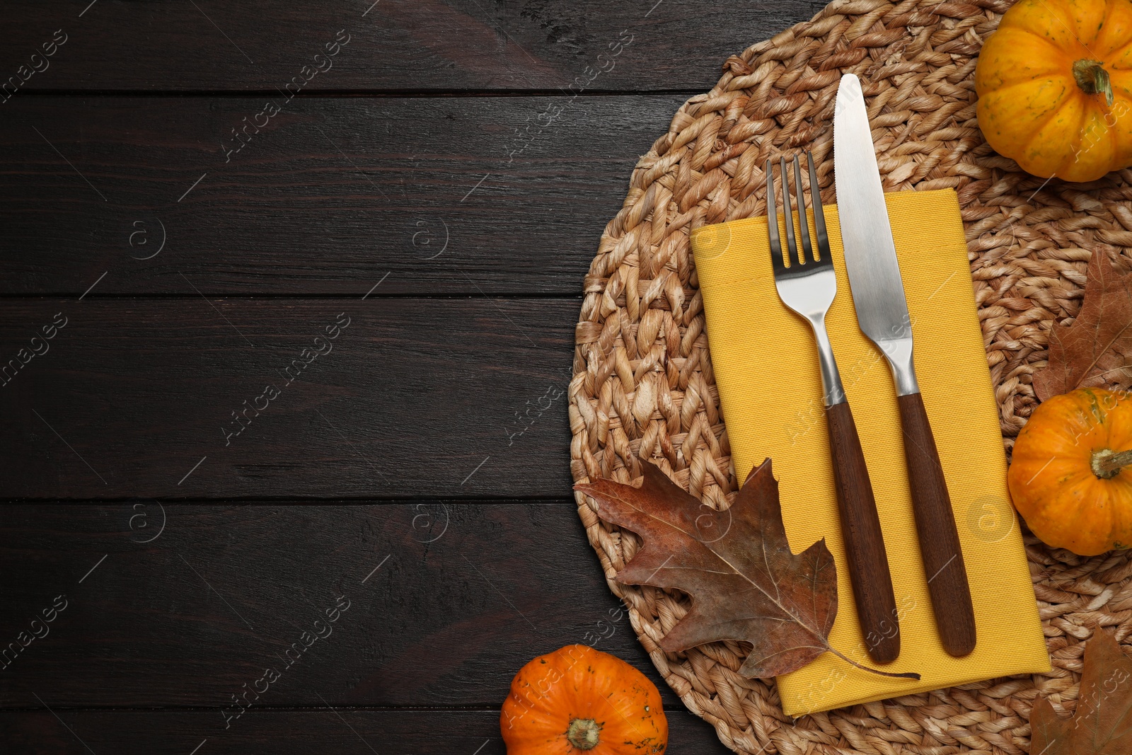 Photo of Cutlery, napkin and autumn decoration on dark wooden background, flat lay with space for text. Table setting