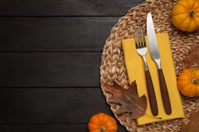 Cutlery, napkin and autumn decoration on dark wooden background, flat lay with space for text. Table setting