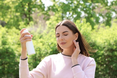 Photo of Young woman applying thermal water on face outdoors. Cosmetic product