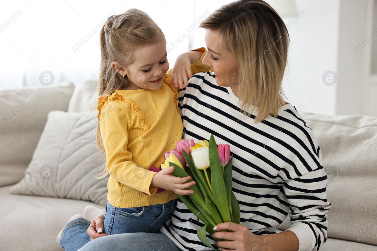 Photo of Little daughter congratulating her mom with Mother`s Day at home. Woman holding bouquet of beautiful tulips