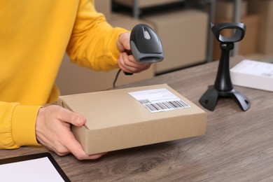 Photo of Seller with scanner reading parcel barcode at workplace, closeup. Online store