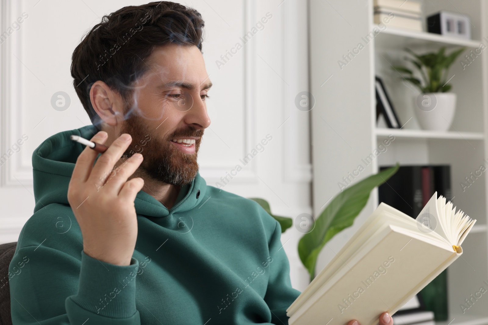 Photo of Man using cigarette holder for smoking white reading book indoors