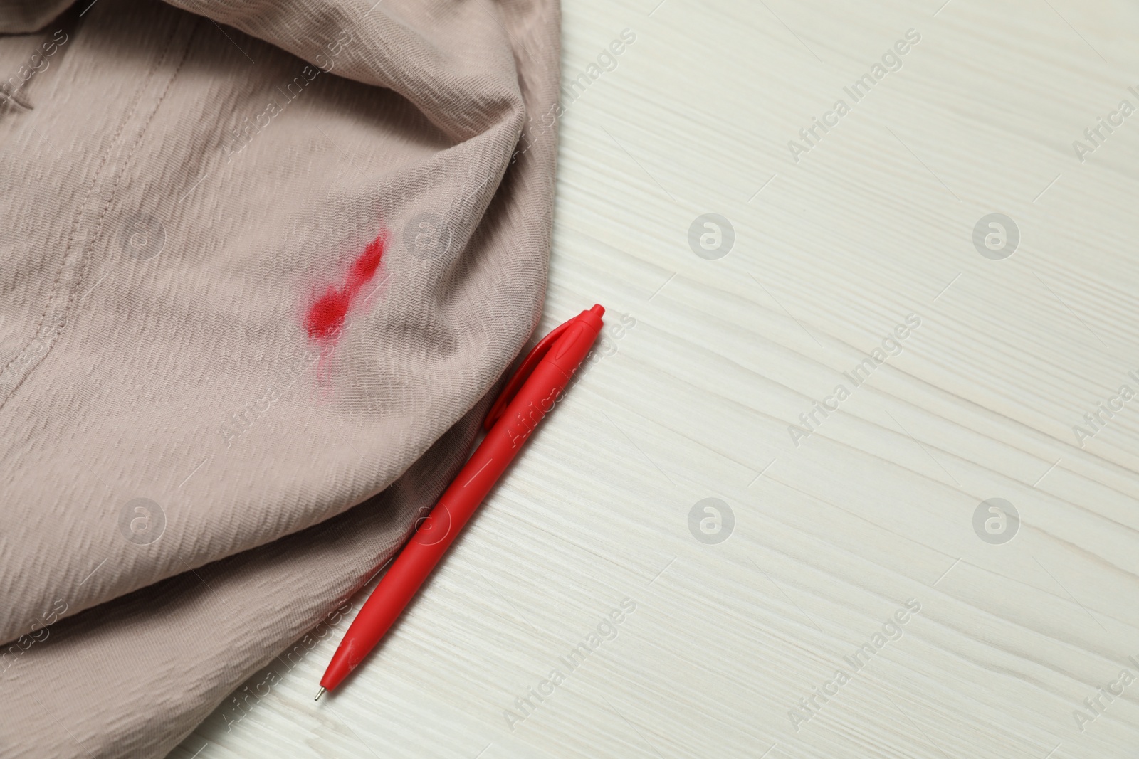 Photo of Clothes with stain of red ink and pen on wooden table, top view. Space for text