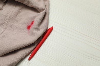 Clothes with stain of red ink and pen on wooden table, top view. Space for text