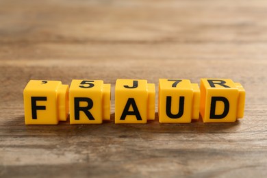 Photo of Word Fraud of yellow cubes with letters on wooden background