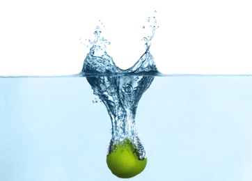 Photo of Ripe green apple falling down into clear water with splashes against white background