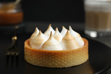 Photo of Tartlet with meringue on black plate, closeup. Delicious dessert