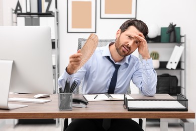 Bearded businessman waving hand fan to cool himself at table in office