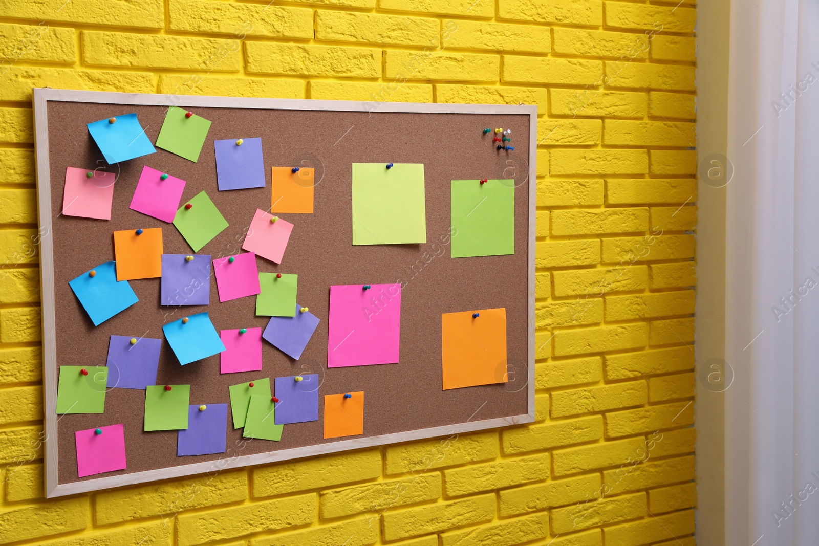 Photo of Corkboard filled with colorful notes and pins on yellow brick wall