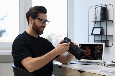 Photo of Professional photographer in glasses holding digital camera at table in office