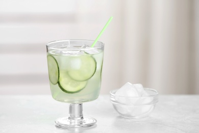 Photo of Glass of tasty cucumber martini cocktail with ice on table against indoors, space for text