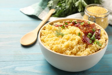 Photo of Tasty millet porridge with bacon, green onion and dill in bowl on light blue wooden table, closeup. Space for text