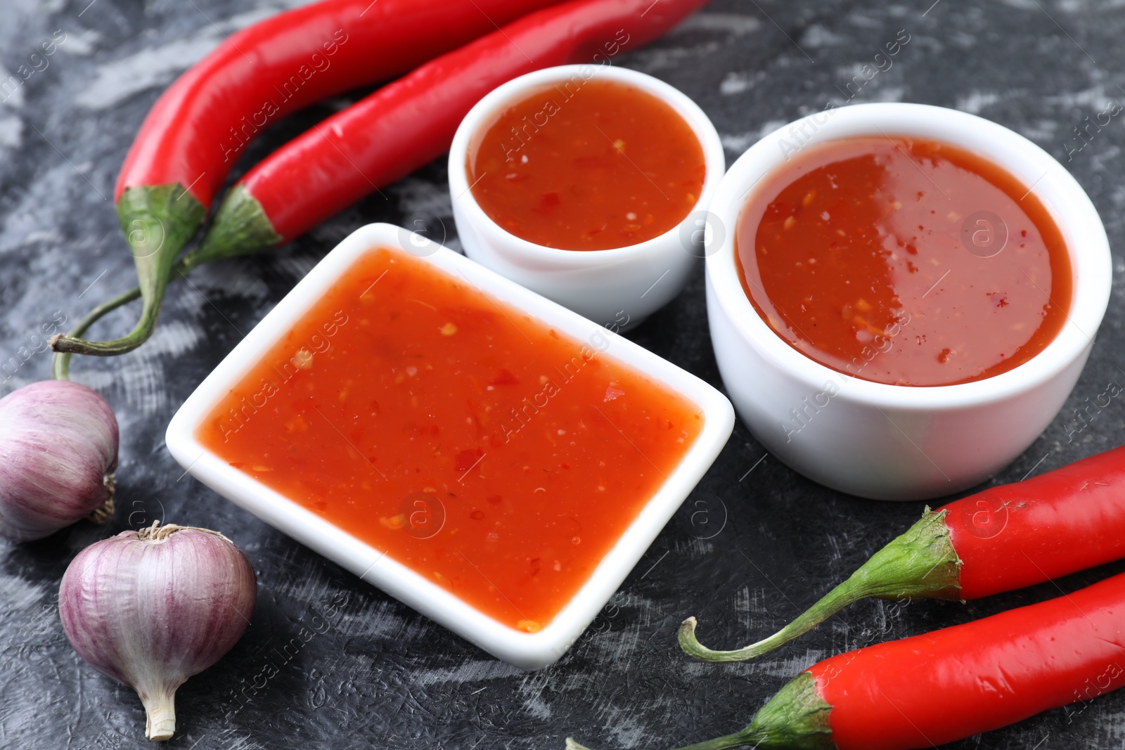 Photo of Spicy chili sauce, peppers and garlic on black textured table, closeup