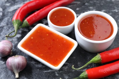 Photo of Spicy chili sauce, peppers and garlic on black textured table, closeup