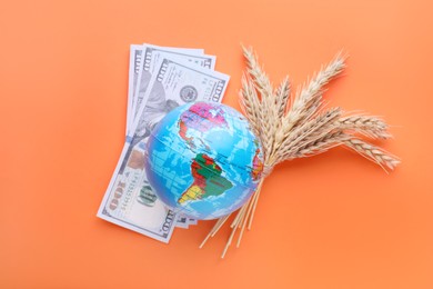 Photo of Import and export concept. Globe, ears of wheat and money on orange background, flat lay