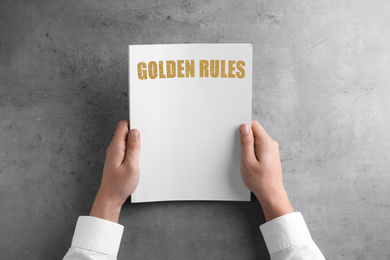 Image of Man holding booklet with phrase GOLDEN RULES at grey table, top view