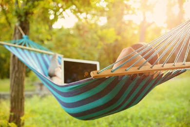 Photo of Young woman with laptop resting in comfortable hammock at green garden