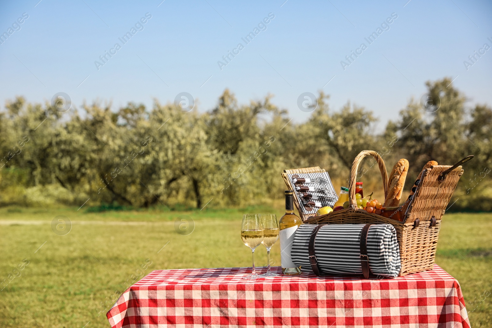 Photo of Picnic basket with wine, snacks and mat on table in park. Space for text