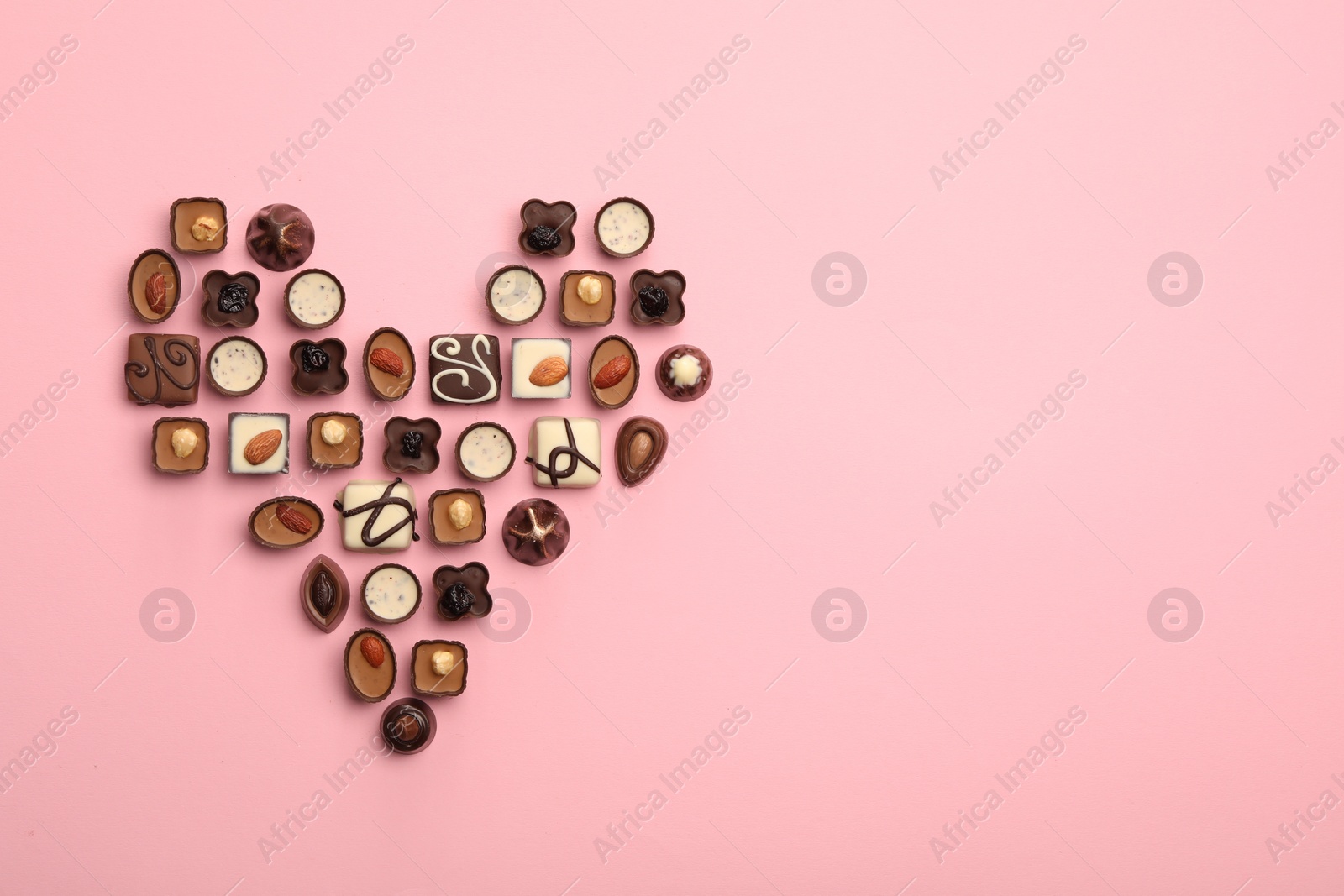 Photo of Heart made with delicious chocolate candies on pink background, top view. Space for text