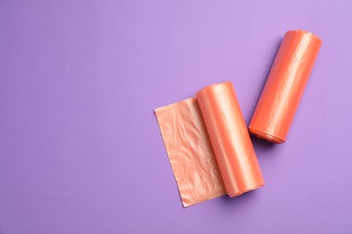 Rolls of orange garbage bags on violet background, flat lay. Space for text