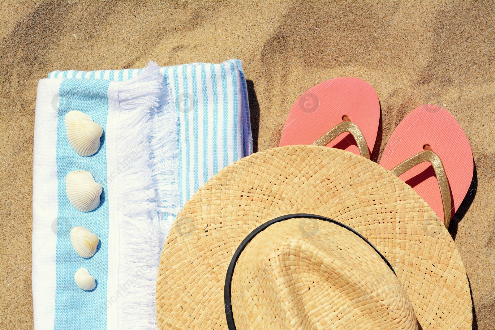 Photo of Straw hat, beach towel, seashells and flip flops on sand, flat lay