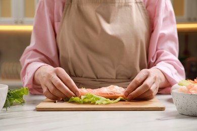 Woman making delicious spring roll at white marble table, closeup