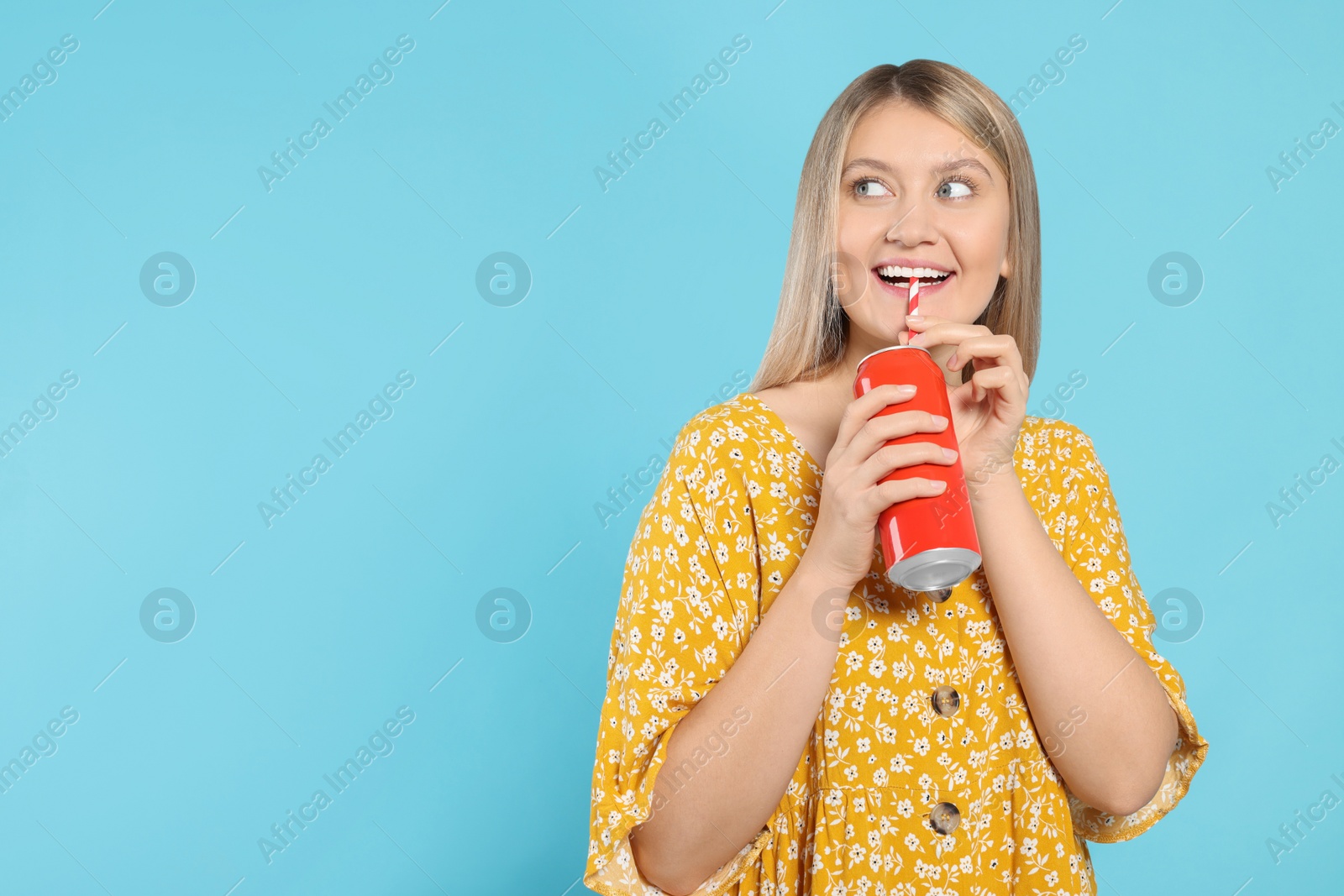 Photo of Beautiful happy woman drinking from red beverage can on light blue background. Space for text