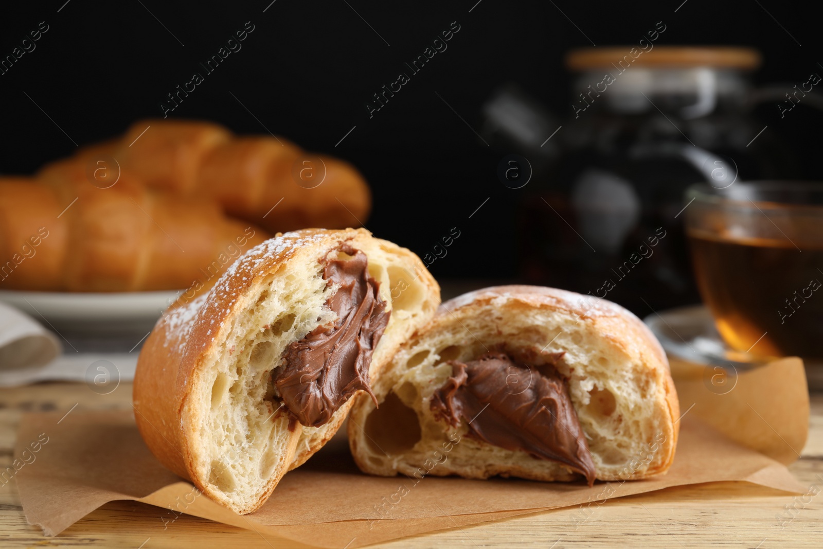 Photo of Tasty croissant with chocolate and sugar powder on wooden table. Space for text