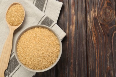 Photo of Brown sugar in bowl and spoon on wooden table, flat lay. Space for text