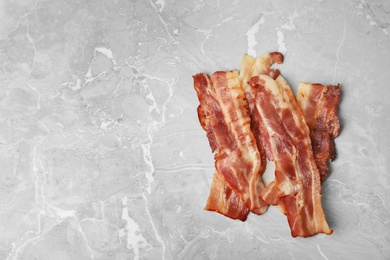 Photo of Slices of tasty fried bacon on light grey marble table, top view. Space for text