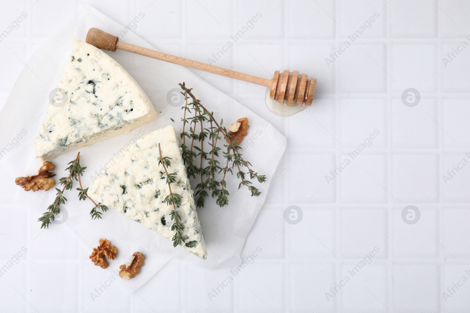 Photo of Tasty blue cheese with thyme, walnuts and honey dipper on white tiled table, flat lay. Space for text