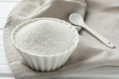 Photo of Granulated sugar in bowl and spoon on white wooden table, closeup