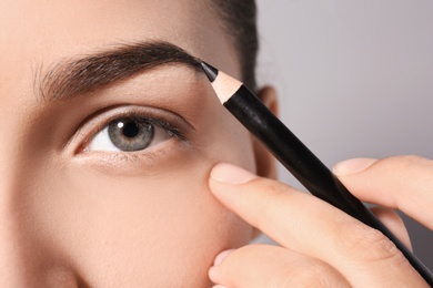 Photo of Young woman correcting eyebrow shape with pencil, closeup