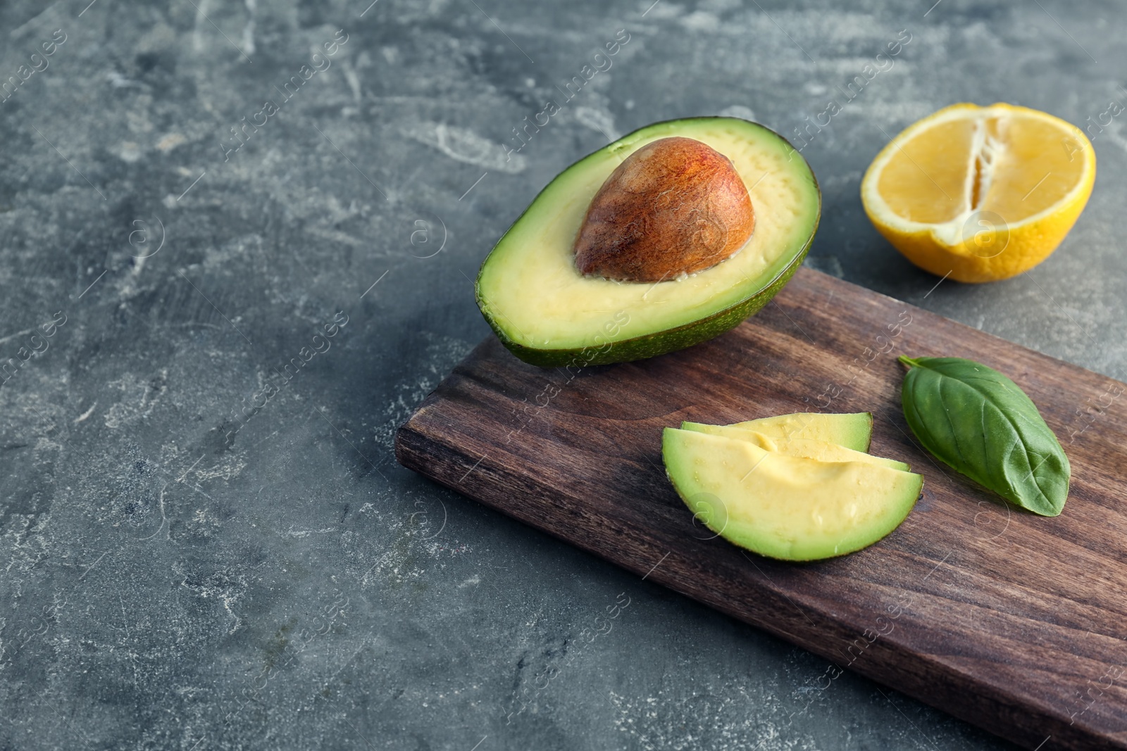 Photo of Wooden board with cut avocado and lemon on grey background