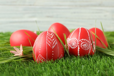 Photo of Red painted Easter eggs on green grass against light background