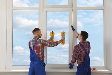 Photo of Workers using suction lifters during plastic window installation indoors