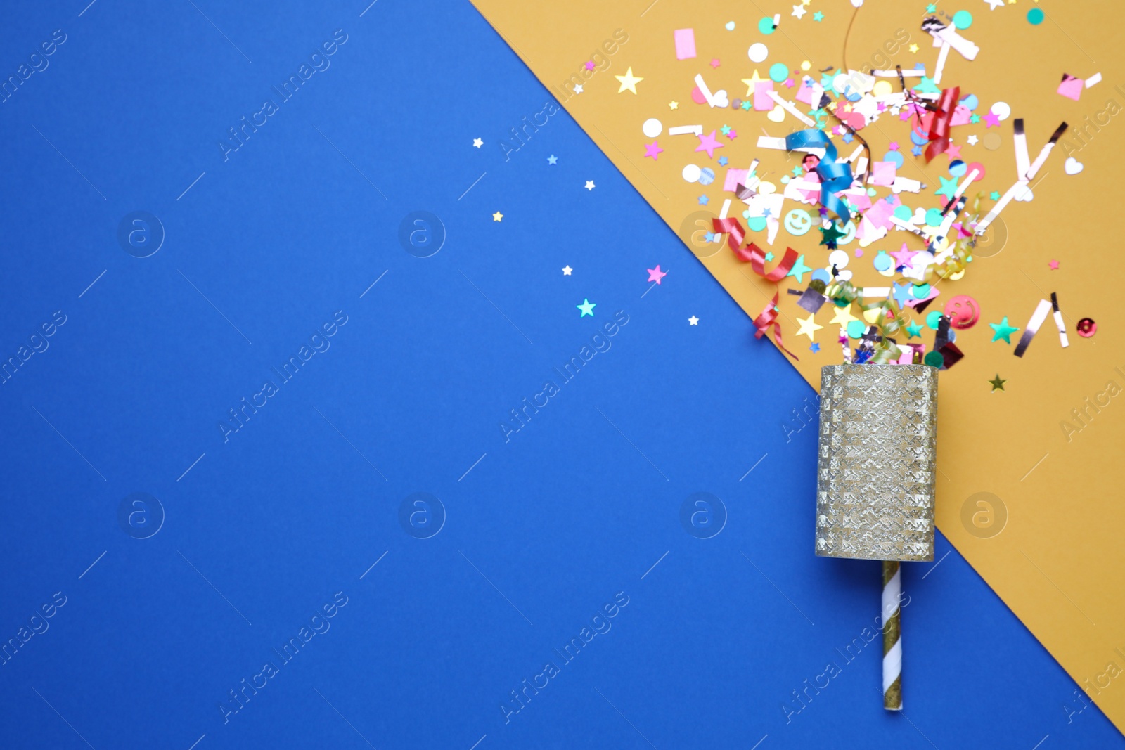 Photo of Shiny confetti and party cracker on color background, top view. Space for text